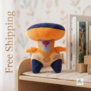 May include: A plush toy shaped like a stylized mushroom with a large, rounded orange cap and a dark blue top. The body is orange with dark blue legs, light blue accents, and a small pink detail on the chest, standing upright on a flat surface.