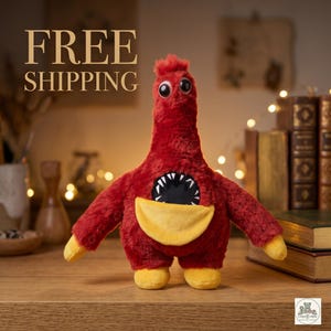 Puede incluir: Un peluche rojo con forma de monstruo con pico y pies amarillos, y una boca negra con dientes blancos. El juguete tiene ojos grandes y redondos y brazos pequeños. El texto "FREE SHIPPING" está en la parte superior de la imagen.