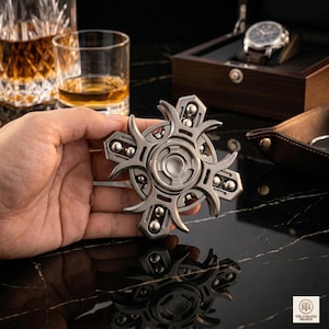 Peut inclure: Un hand spinner argenté avec un design géométrique complexe. Le spinner comporte plusieurs bras avec de petites billes argentées. L'arrière-plan comprend une montre, un plateau et des verres de liquide ambré, suggérant un thème de luxe.