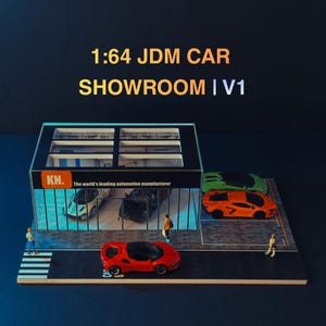 May include: A 1:64 scale JDM car showroom model featuring a black building with glass walls, an orange sign labelled KN, and the text The world's leading automotive manufacturer. Includes miniature cars in red, orange, and green, plus small figures.