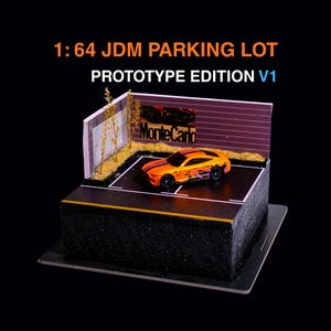 May include: A 1:64 scale JDM parking lot prototype edition V1 diorama featuring a miniature orange sports car with black and purple graphics parked on a black asphalt surface with white lines, a wall with a Monte Carlo sign, and small trees.
