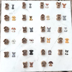 Dog breed polymer clay cutters paired with matching colorful clay cutouts on a white marble surface, showing all twenty-two breed designs side by side.