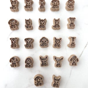 Twenty-two dog breed polymer clay cutters arranged in rows on a white marble surface showing a wide variety of sitting puppy designs.