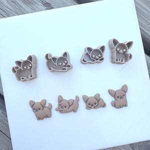 May include: A set of eight light brown plastic cookie cutters shaped like small dogs in various poses, including sitting, lying down, and standing. The cutters feature detailed outlines of ears, faces, and bodies with a smooth, matte finish.