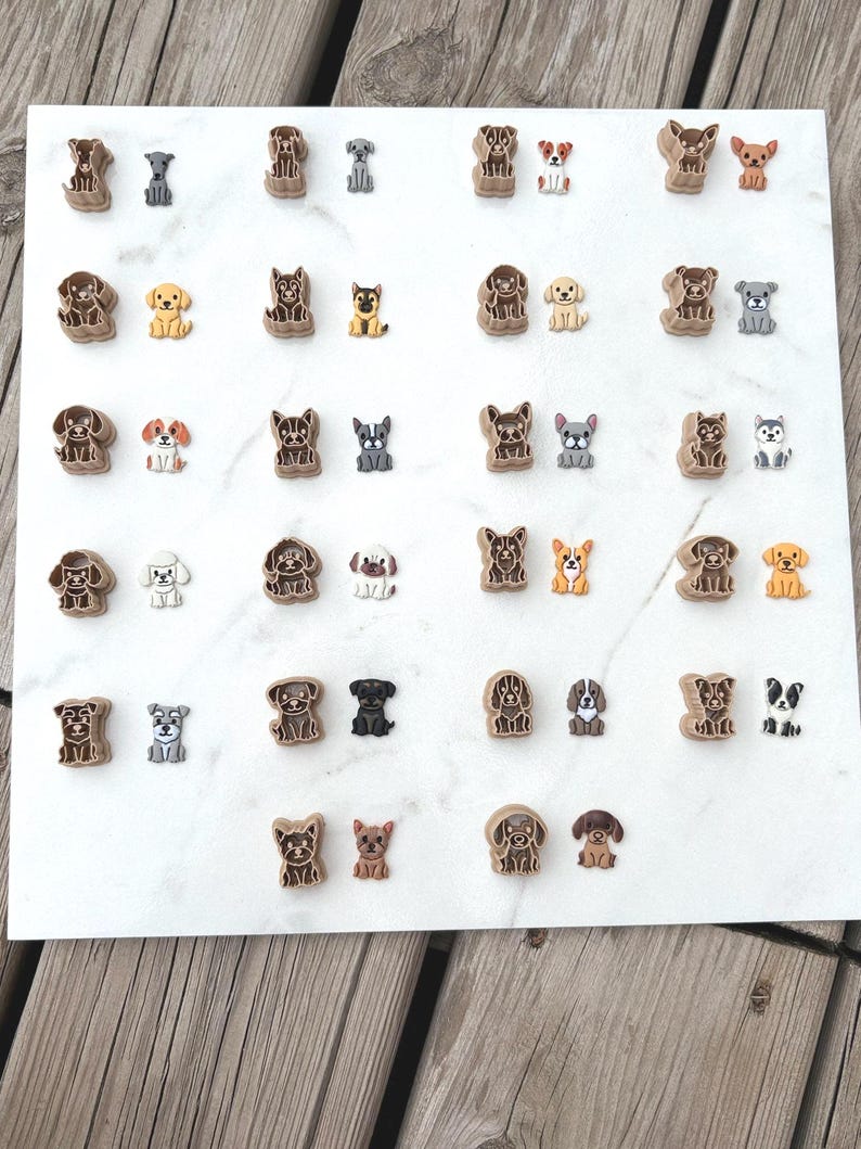 Dog breed polymer clay cutters paired with matching colorful clay cutouts on a white marble surface, showing all twenty-two breed designs side by side.