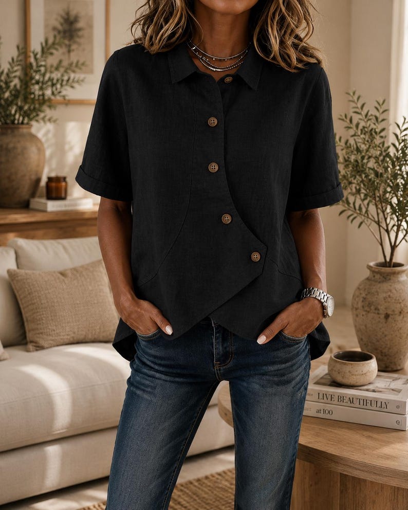 May include: A black short-sleeved shirt with a collar and a unique asymmetrical button-down front closure featuring light brown buttons. The shirt has a straight hemline and is paired with blue denim jeans, creating a casual and functional outfit.