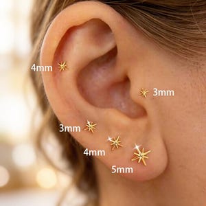 Puede incluir: Una colección de pendientes dorados en forma de estrella, que varían en tamaño de 3 mm a 5 mm. Los pendientes se muestran en una oreja, destacando sus diferentes tamaños y diseños. Un accesorio sencillo pero elegante.