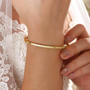 Puede incluir: Una pulsera dorada con la inscripción grabada "feelings are not facts". La pulsera tiene un diseño de brazalete abierto y sencillo. La imagen muestra la pulsera en la muñeca de una persona.