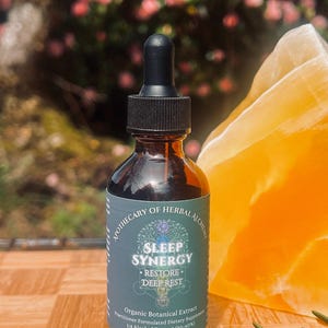 May include: A brown glass bottle with a black dropper, labeled "SLEEP SYNERGY" and "RESTORE DEEP REST". The bottle contains a liquid extract, with a 2 fl oz (60 mL) volume. The background includes a yellow crystal and greenery.