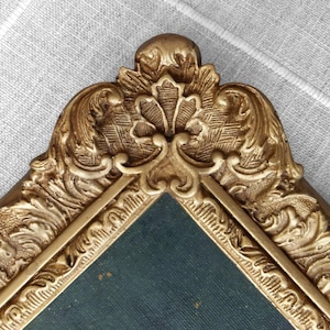 Close up of gold toned frame featuring elaborate floral detailing.