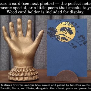 K&ouml;nnte beinhalten: Ein goldfarbener kartenhalter in Handform mit ger&uuml;schtem Sockel, der eine blaue Karte mit einem goldenen Mond- und Baumdesign h&auml;lt. Der Text lautet: "W&auml;hlen Sie eine Karte...Kartenhalter aus Holz ist im Lieferumfang enthalten."
