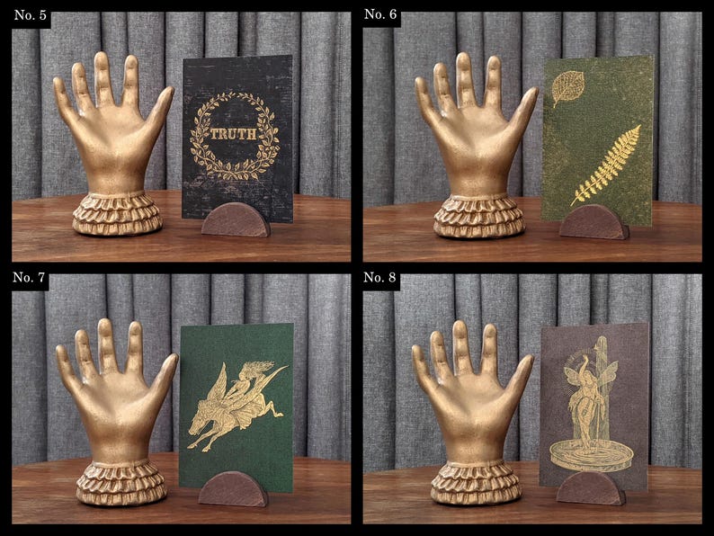 K&ouml;nnte beinhalten: Vier Bilder zeigen dekorative goldene Handskulpturen mit ger&uuml;schtem Sockel. Jede Hand h&auml;lt eine Karte in einem braunen Halter. Die Karten zeigen verschiedene Designs: "TRUTH" in einem Kranz, botanische Drucke, ein gefl&uuml;geltes Pferd und eine klassische Figur.