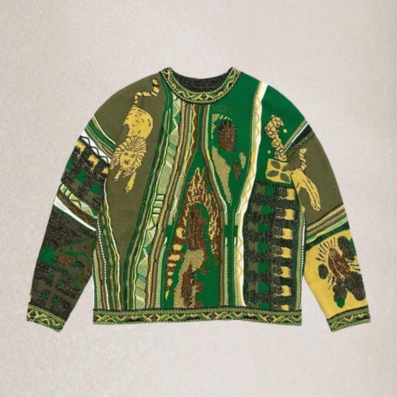 May include: A green, brown, and yellow crew neck sweater. The garment displays a variety of patterns and images, including a lion, geometric shapes, and abstract designs. The sleeves are long and the overall style is oversized.