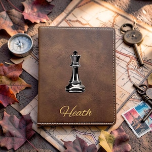 May include: A brown rectangular passport holder featuring a black chess king piece graphic centered on the front cover. The name Heath is printed in a gold cursive font below the chess piece. The cover has visible white stitching.