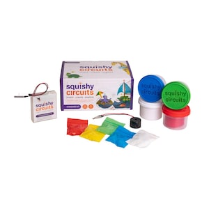 May include: A white ceramic mug with a black handle and the text "But First, Coffee" in a bold, black font. The mug is set against a blurred background, suggesting a cozy setting.