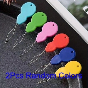 May include: A collection of six colorful needle threaders in shades of blue, green, pink, red, blue, and yellow. Each threader has a teardrop-shaped handle and a thin wire loop. The text "2Pcs Random Colors" is visible.