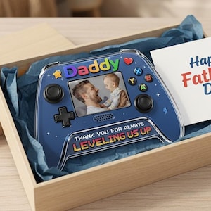 May include: A blue video game controller with the word "Daddy" and a photo inside a wooden box. The controller has the text "THANK YOU FOR ALWAYS LEVELING US UP". A card reads "Happy Father's Day".