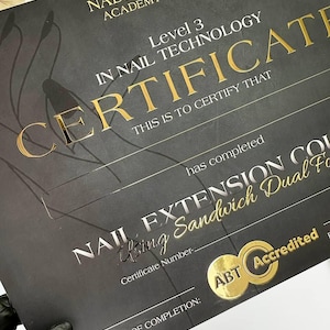 Peut inclure: Un certificat noir avec des lettres dorées de Nadiia Gumeniuk Academy & Beauty. Le certificat est pour le niveau 3 en technologie des ongles et comprend le texte "Nail Extension Course Using Sandwich Dual Form". Un sceau ABT Accredited est visible.