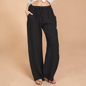 Puede incluir: Pantalones negros de pernera ancha con cintura con cordón y bolsillos laterales. Los pantalones están hechos de una tela ligera y tienen un ajuste relajado. Los pantalones se muestran con sandalias.