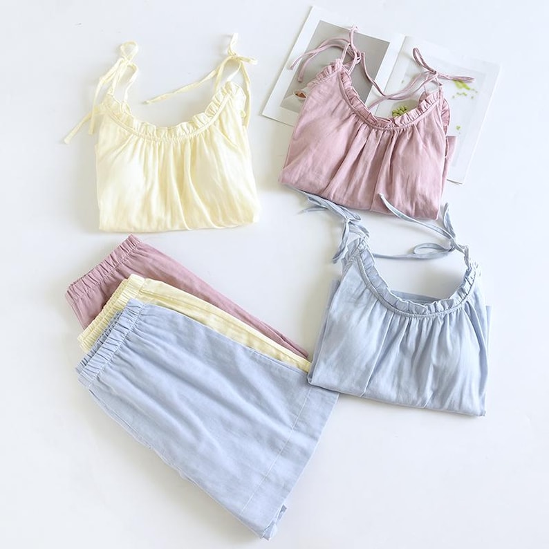 May include: A collection of pastel-colored sleepwear sets. The sets include tops with tie straps and ruffled necklines, paired with matching elastic-waist shorts. Colors include pale yellow, lavender, and light blue. The fabric appears soft and lightweight.