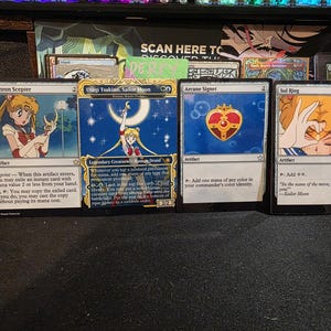 May include: Four Magic: The Gathering cards featuring Sailor Moon artwork. The cards include "Isochron Scepter", "Usagi Tsukino, Sailor Moon", "Arcane Signet", and "Sol Ring". The cards are displayed on a dark surface.