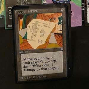 Könnte beinhalten: Eine Magic: The Gathering-Karte mit dem Titel "Copper Tablet". Die Karte zeigt eine Illustration einer Zeichnung auf einer Steintafel. Der Text lautet: "Zu Beginn jedes Unterhalts des Spielers fügt dieses Artefakt dem Spieler 1 Schaden zu."