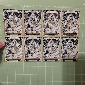 May include: Eight identical rectangular trading cards arranged in two rows of four. Each card features a black, white, and gold illustration of a figure surrounded by treasure, with the word TREASURE printed at the top and game text at the bottom.