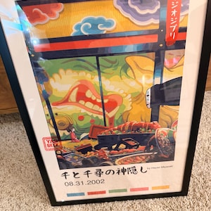 Puede incluir: Impresi&oacute;n art&iacute;stica enmarcada con una colorida ilustraci&oacute;n y texto japon&eacute;s. La obra de arte representa una escena con comida, una peque&ntilde;a figura y una gran criatura. La impresi&oacute;n incluye el texto "千と千尋の神隠し" y "08.31.2002".