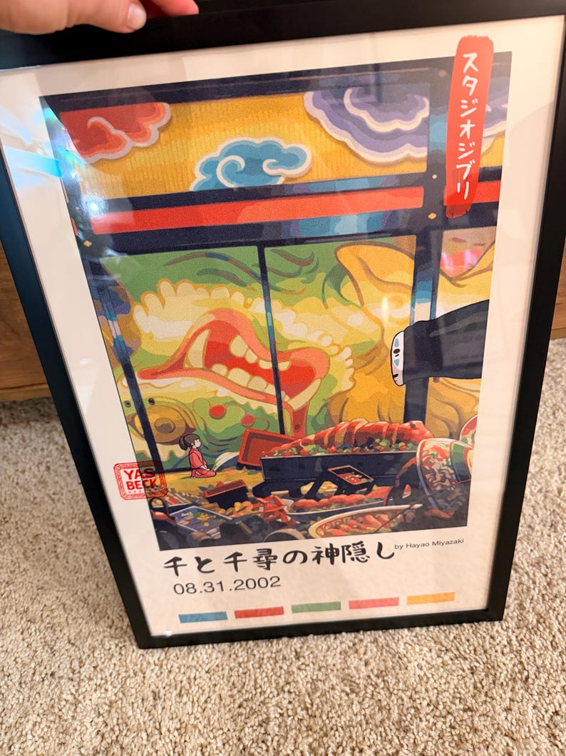 Puede incluir: Impresi&oacute;n art&iacute;stica enmarcada con una colorida ilustraci&oacute;n y texto japon&eacute;s. La obra de arte representa una escena con comida, una peque&ntilde;a figura y una gran criatura. La impresi&oacute;n incluye el texto "千と千尋の神隠し" y "08.31.2002".