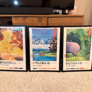 Pu&ograve; includere: Tre stampe artistiche di anime incorniciate. Le stampe presentano illustrazioni colorate con testo e date in giapponese. Le cornici sono nere e le stampe sono esposte su un tappeto di colore chiaro.