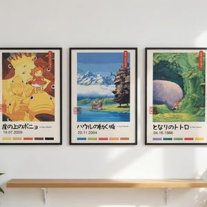 Pu&ograve; includere: Tre stampe artistiche incorniciate con scene di animazione giapponese. Le cornici nere racchiudono illustrazioni colorate con testo e date in giapponese. Sono esposte su una parete bianca sopra una mensola di legno.