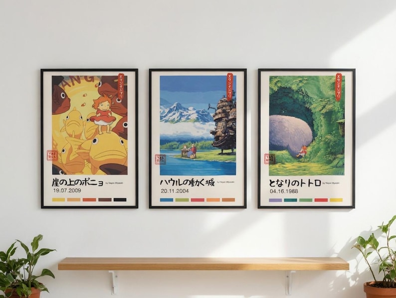 Pu&ograve; includere: Tre stampe artistiche incorniciate con scene di animazione giapponese. Le cornici nere racchiudono illustrazioni colorate con testo e date in giapponese. Sono esposte su una parete bianca sopra una mensola di legno.