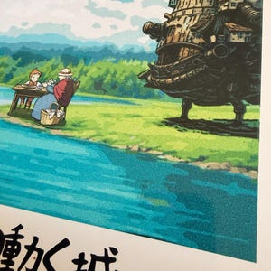 Op de afbeelding: Kleurrijke illustratie met een sc&egrave;ne uit een film. Een groot, gedetailleerd, bewegend kasteel staat rechts. Een rivier stroomt op de voorgrond, met een bergketen op de achtergrond. Tekst in het Japans en Engels onderaan.