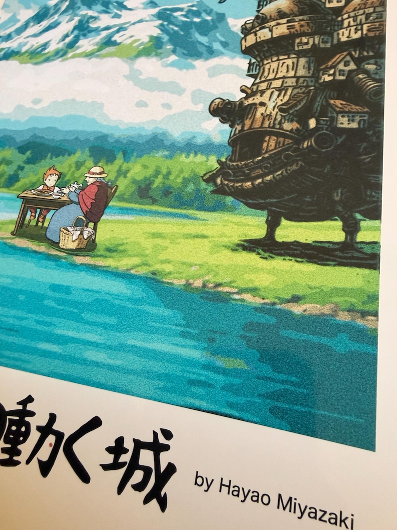 Op de afbeelding: Kleurrijke illustratie met een sc&egrave;ne uit een film. Een groot, gedetailleerd, bewegend kasteel staat rechts. Een rivier stroomt op de voorgrond, met een bergketen op de achtergrond. Tekst in het Japans en Engels onderaan.