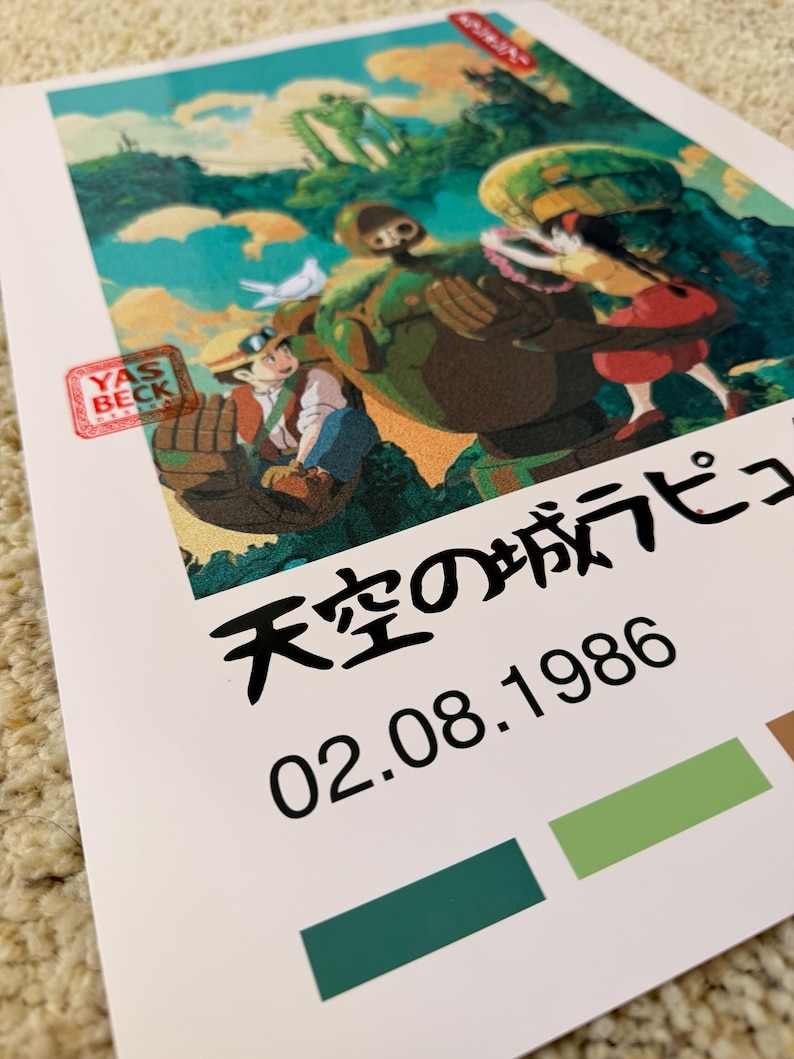 May include: A print with a vibrant illustration from an animated film. The artwork shows characters and a robot in a mountainous setting. Japanese text and the date 02.08.1986 are printed below the image. A red stamp with the text "YAS BECK" is in the lower left corner.