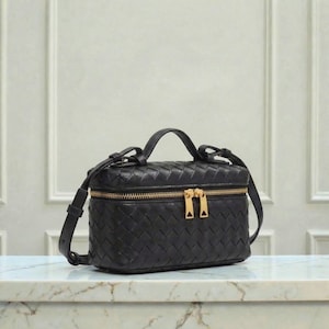 May include: Black leather crossbody bag with a woven design. The bag has a rectangular shape with a top handle and a long adjustable strap. It features a gold-tone zipper and hardware.