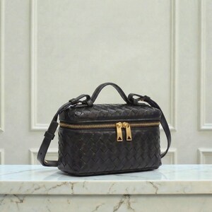 May include: Black leather handbag with a woven design. The bag has a rectangular shape with a top handle and a detachable shoulder strap. It features a gold-colored zipper and hardware.