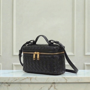 May include: Black leather crossbody bag with a woven design. The bag has a rectangular shape with a top handle and a long, adjustable strap. It features a gold-tone zipper closure and hardware.