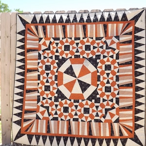 May include: A quilt with a geometric pattern in black, white, orange, and brown. The quilt is made up of repeating triangles, squares, and circles.