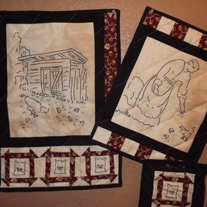 May include: Three framed black and white embroidered pictures with red and white patterned borders. The pictures depict a small building, a person feeding chickens, and a bag of feed.