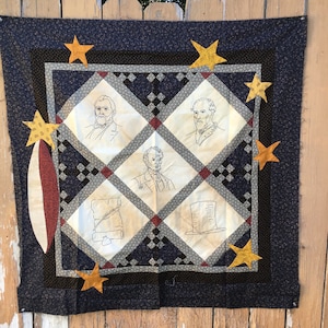 May include: A blue and white quilt with a black border. The quilt features a grid pattern with stars and images of historical figures. The images are in black and white and include Abraham Lincoln, Ulysses S. Grant, and Robert E. Lee.