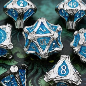 May include: Set of silver and blue polyhedral dice with white numbering. The dice are designed with a metallic finish and blue enamel accents. The image includes the text "C001" and "Call of Cthulhu". The dice are for tabletop gaming.