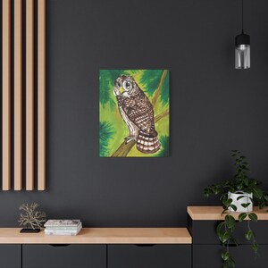 May include: A canvas print featuring a detailed painting of a brown and white owl perched on a branch. The owl has yellow eyes and is set against a green background with painted foliage. The artwork is displayed on a dark gray wall.