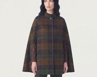May include: A plaid cape featuring a brown, green, and dark blue tartan pattern. The garment has a high collar, a front button closure with four visible buttons, and arm slits on the sides. It is worn over a solid brown long-sleeved top.