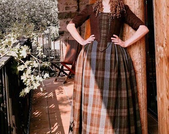 May include: A woman wearing a brown plaid skirt and matching bodice with short sleeves. The bodice has a laced front and is paired with a long, full skirt in shades of brown, gray, and blue. The outfit is reminiscent of historical attire.