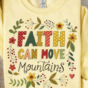 Puede incluir: Una sudadera de cuello redondo de color amarillo pálido con el texto FAITH CAN MOVE MOUNTAINS en letras de bloque coloridas y estampadas. El diseño está rodeado por un borde decorativo de flores, hojas y bayas ilustradas en rojo, verde y amarillo.