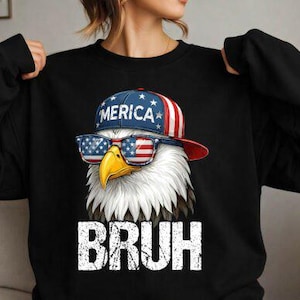 以下が含まれることがあります： サングラスと「MERICA」の文字が入った帽子をかぶったワシのグラフィックが特徴の黒いスウェットシャツ。ワシは黄色いクチバシと白い羽を持っています。「BRUH」の文字がワシの下にプリントされています。