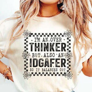 Könnte beinhalten: Cremefarbenes T-Shirt mit einem schwarz-weißen Karomuster und dem Text "I'M AN OVER THINKER BUT ALSO AN IDGAFER SO IT BALANCES OUT". Das Design enthält Gänseblümchen-Akzente.