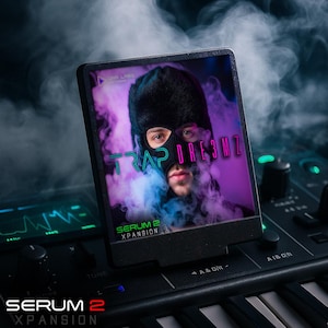 May include: A black electronic device displays a person wearing a black balaclava with the text "TRAP DRE3MZ". The device is on a keyboard with the text "SERUM 2 XPANSION". The background features purple and blue smoke.
