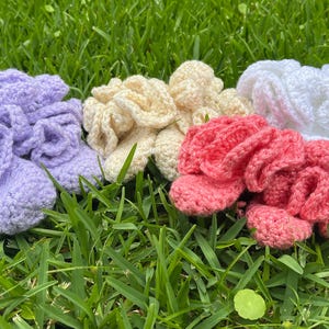 May include: Four pairs of crocheted booties in lavender, cream, coral, and white. Each pair features a ruffled, textured design with a soft, yarn-based construction. The booties are arranged in a row, showcasing their distinct colors and intricate, looped stitch patterns.